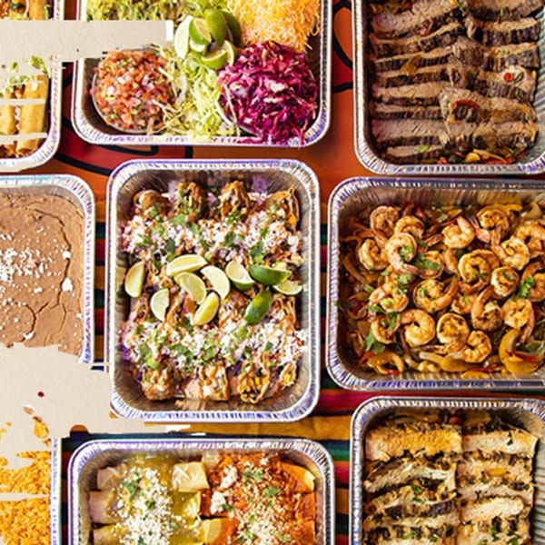 Los Jefes Grill catering spread with various Mexican dishes in foil pans, including meats, shrimp, and sides.