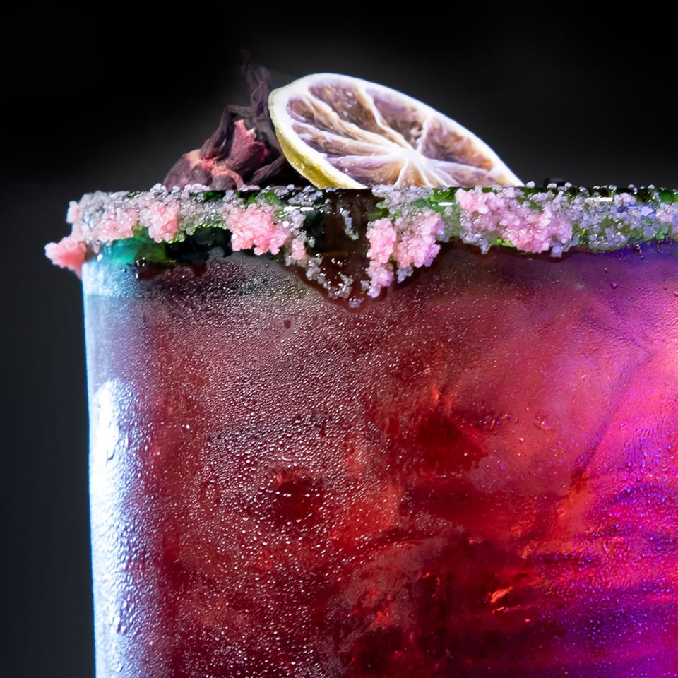 A vibrant red Los Jefes Grill cocktail with a sugared rim and a dried lime slice.