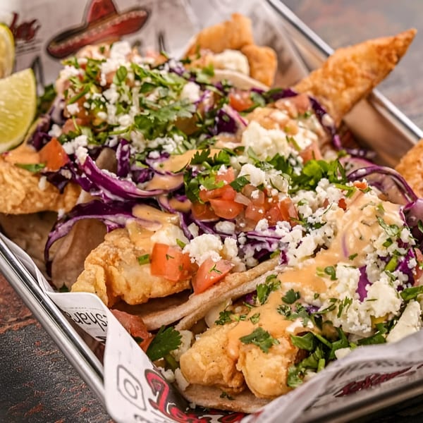 Los Jefes Grill fish tacos with red cabbage, pico de gallo, cotija cheese, and sauce.