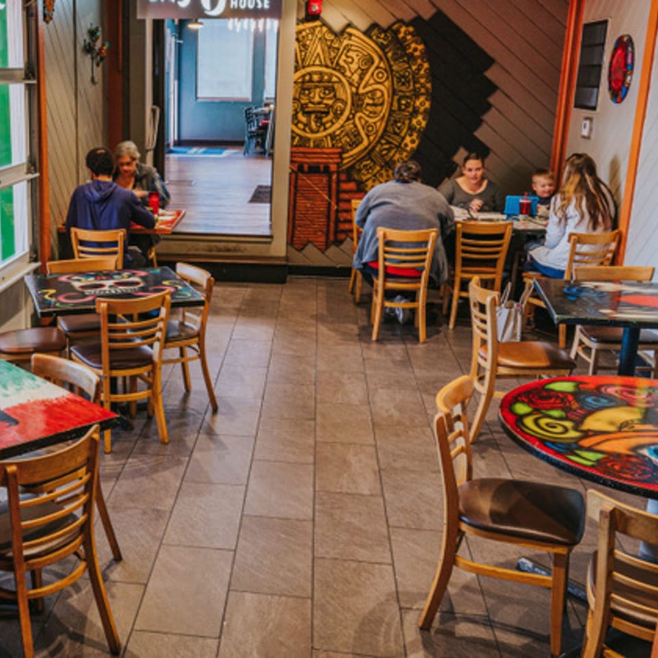 Diners seated at colorful tables in Los Jefes Grill, with a large Aztec calendar mural on the wall.