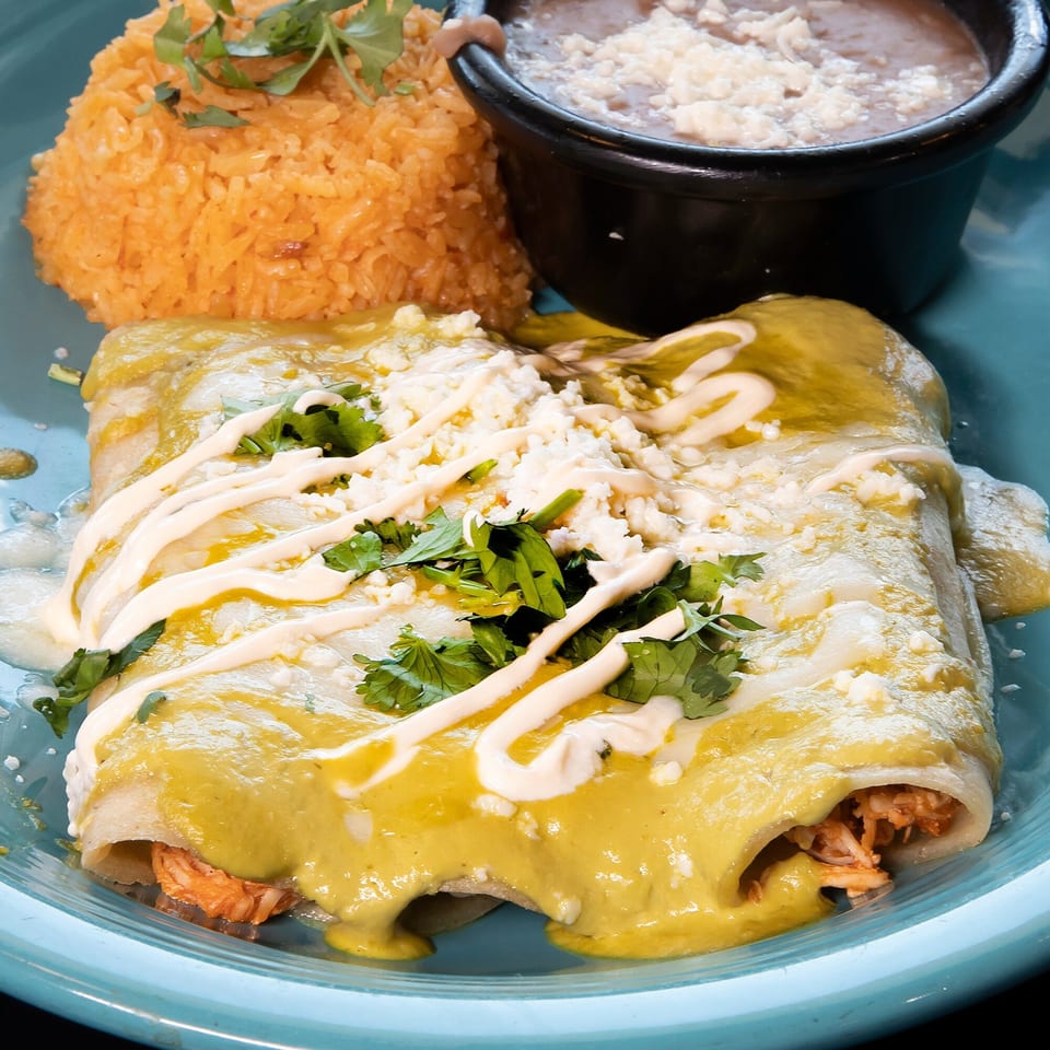 Los Jefes Grill's chicken enchiladas with green sauce, rice, and refried beans on a blue plate.