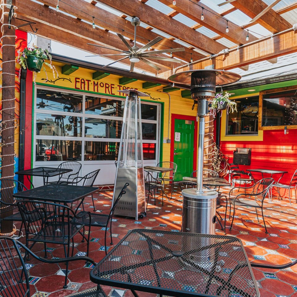 Los Jefes Grill's vibrant outdoor patio with black metal tables, chairs, and heaters on a tiled floor.