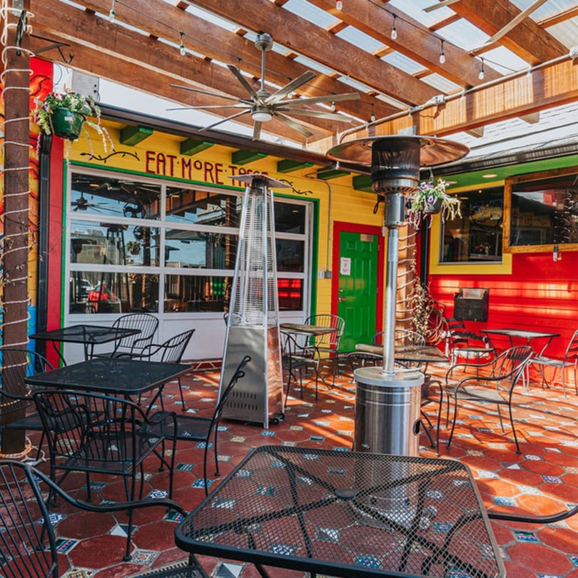 Los Jefes Grill's vibrant outdoor patio with black metal tables, chairs, and heaters on a tiled floor.