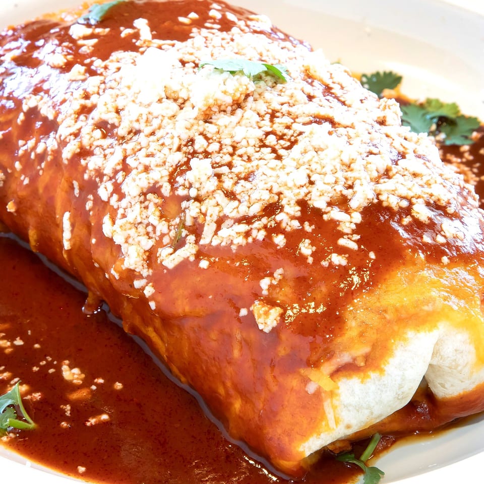 A large, saucy burrito from Los Jefes Grill, topped with crumbled white cheese and cilantro.
