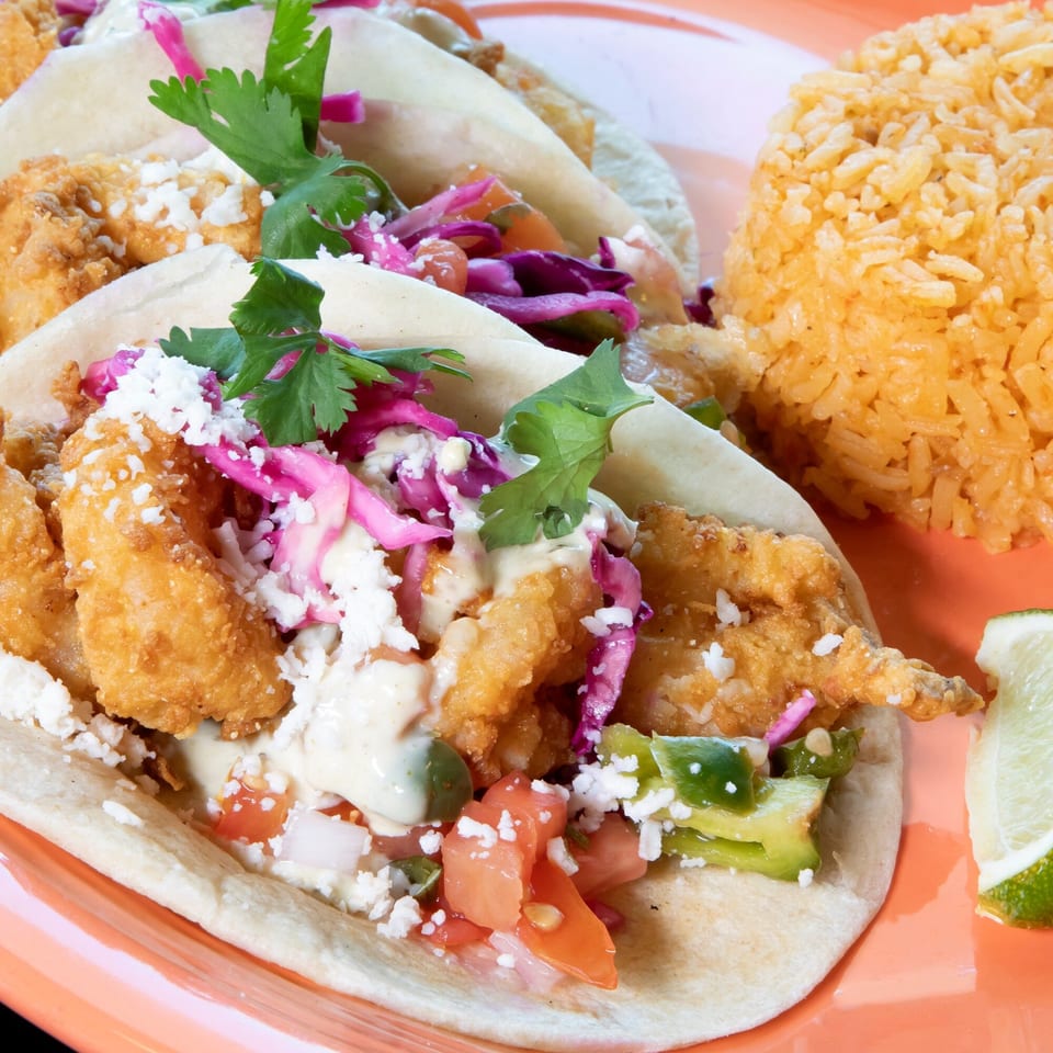 Three Los Jefes Grill fish tacos with red cabbage, cilantro, and rice on an orange plate.