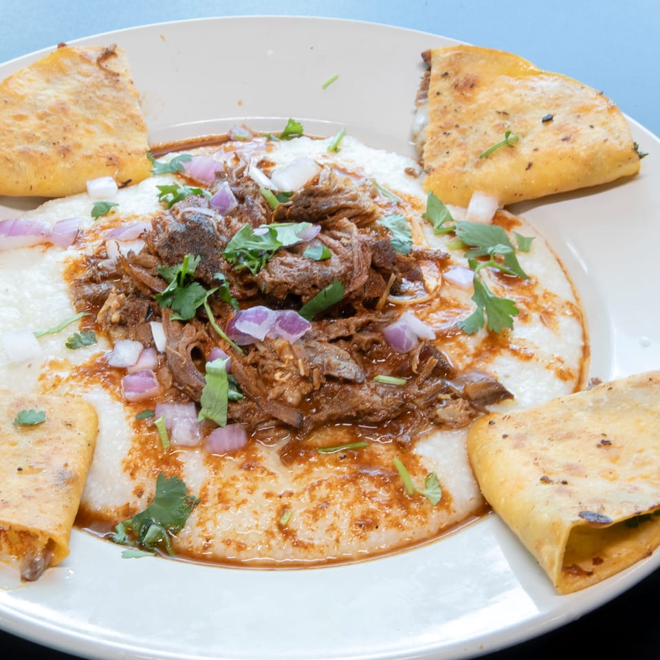 Los Jefes Grill birria tacos and grits, garnished with cilantro and red onions.