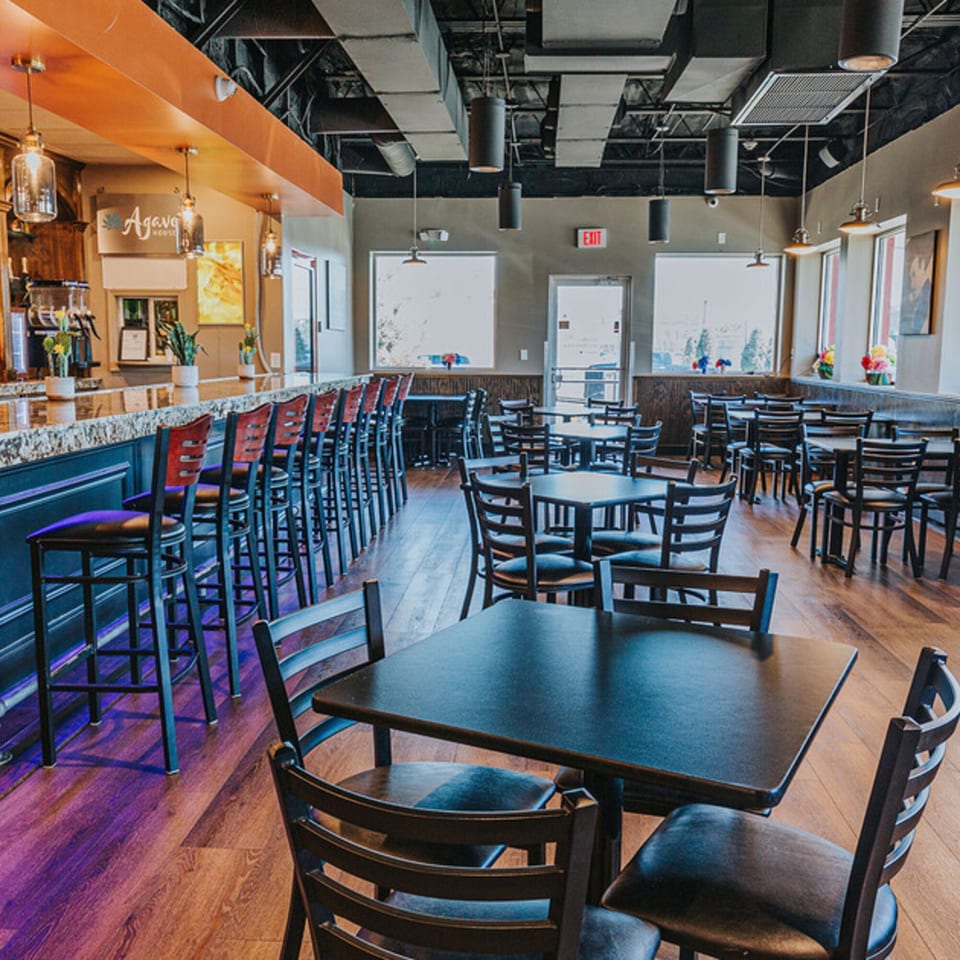 Interior of Los Jefes Grill, showing a long bar with stools and dining tables with chairs.
