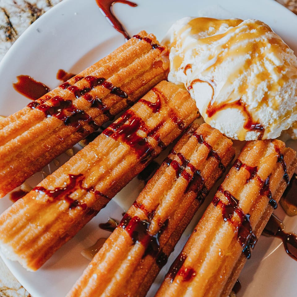 Four churros drizzled with chocolate and caramel, served with a scoop of vanilla ice cream.