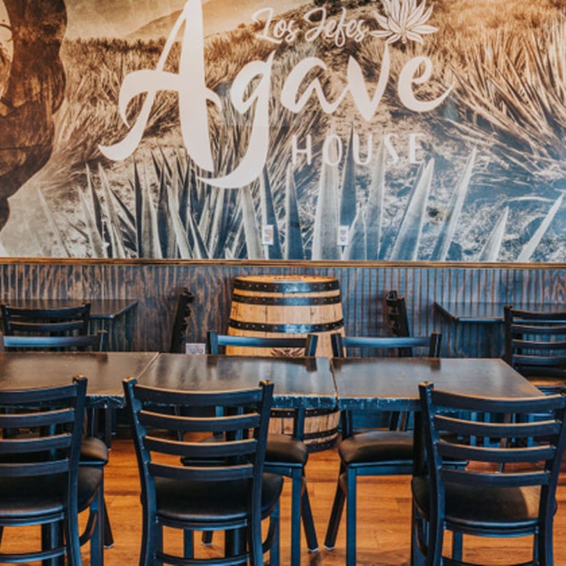 Los Jefes Agave House restaurant interior with tables, chairs, and a barrel against a mural.