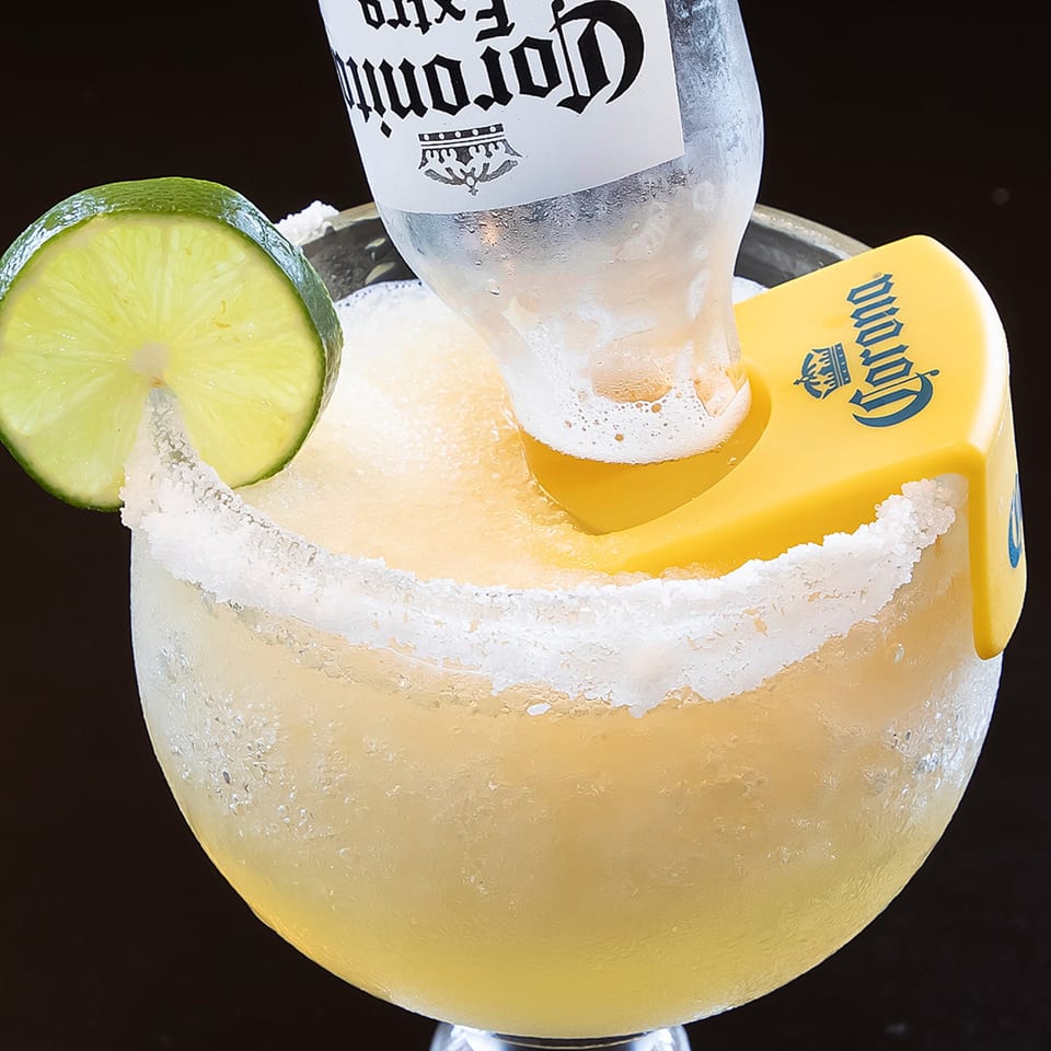 A frozen Los Jefes Grill margarita with a Corona beer bottle inverted into it, garnished with a lime.