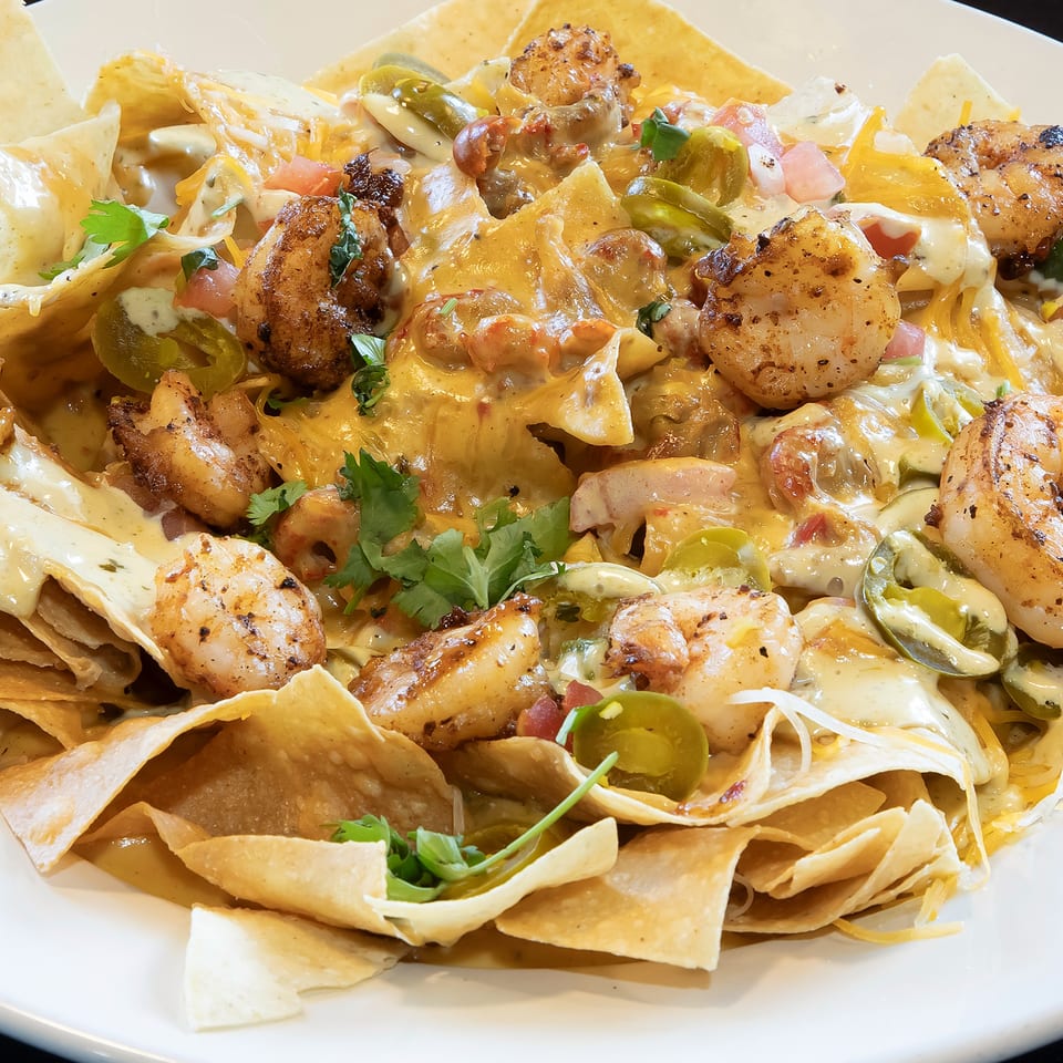 Los Jefes Grill's shrimp nachos, loaded with cheese, jalapeños, and cilantro on a white plate.