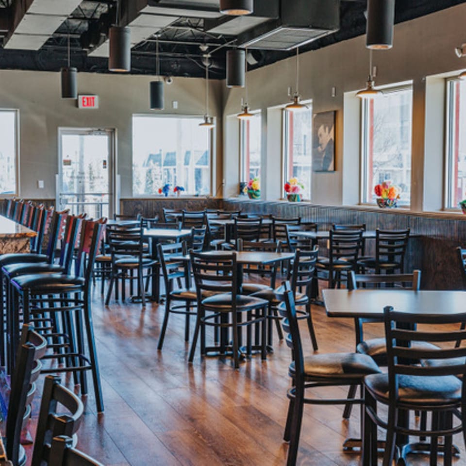 Interior of Los Jefes Grill, showing empty dining tables, chairs, and bar stools with wooden floors.