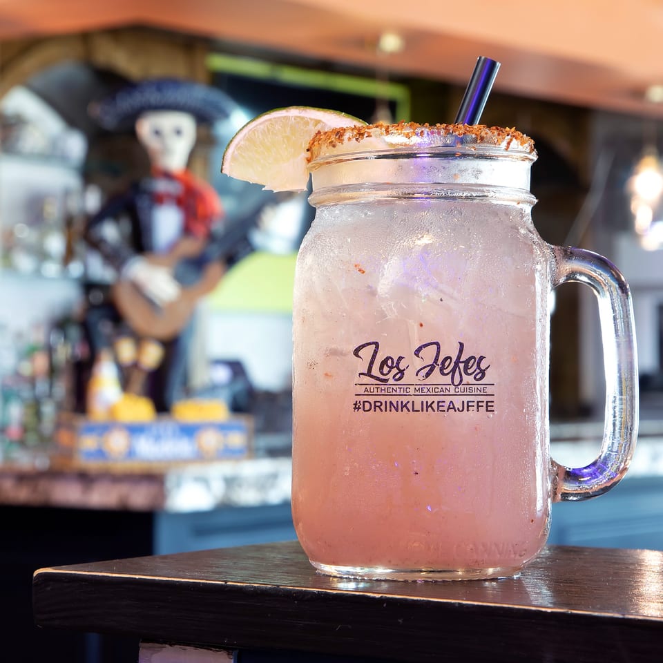 A Los Jefes Grill margarita in a mason jar with a lime wedge and chili salt rim.